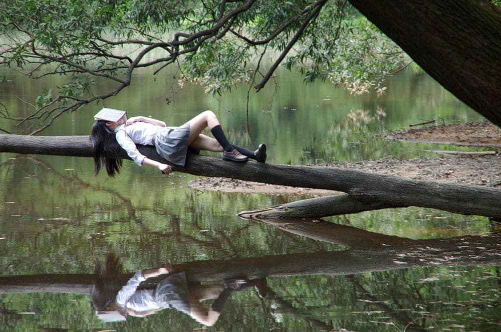 girl falling asleep with book on head outside