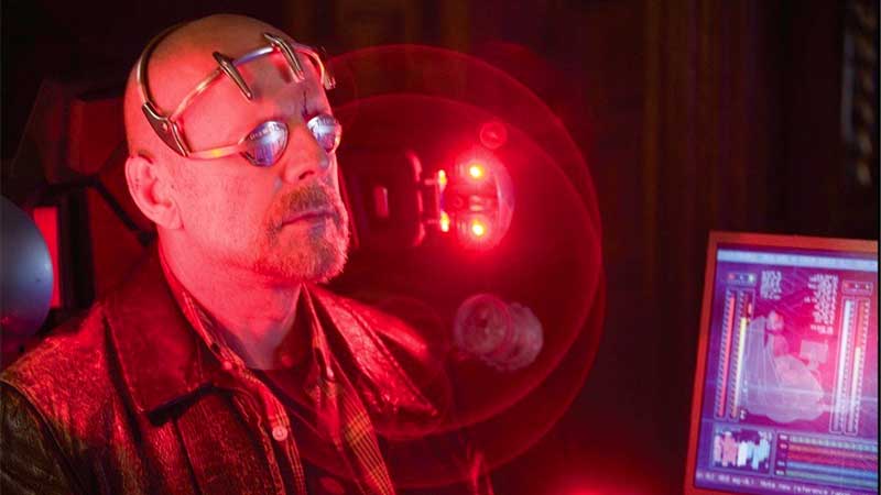 a still photo from surrogates starring bruce willis, sitting in a chair as part of a VR pod with goggles on and a red light behind him - TV Adaptations: 10 Terrible Movies That Could Be Great Shows